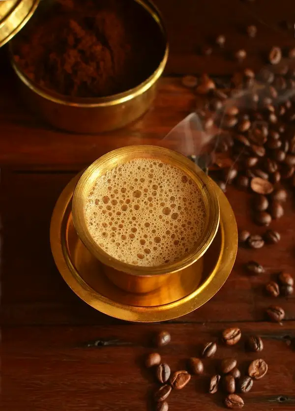 Filter coffee in a brass davara tumbler with coffee beans