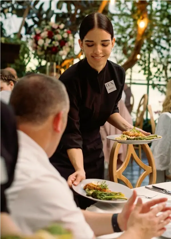 Server presenting plated food to seated guests